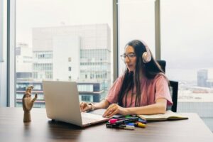 Femme au casque devant un ordinateur, entourée de carnets et feutres